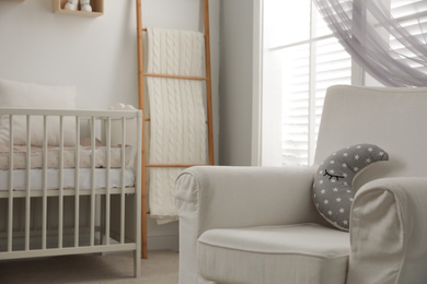Photo of Stylish baby room interior with crib and armchair