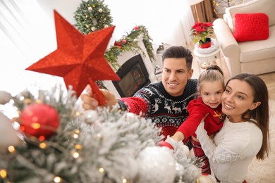 Family decorating Christmas tree with star topper in room