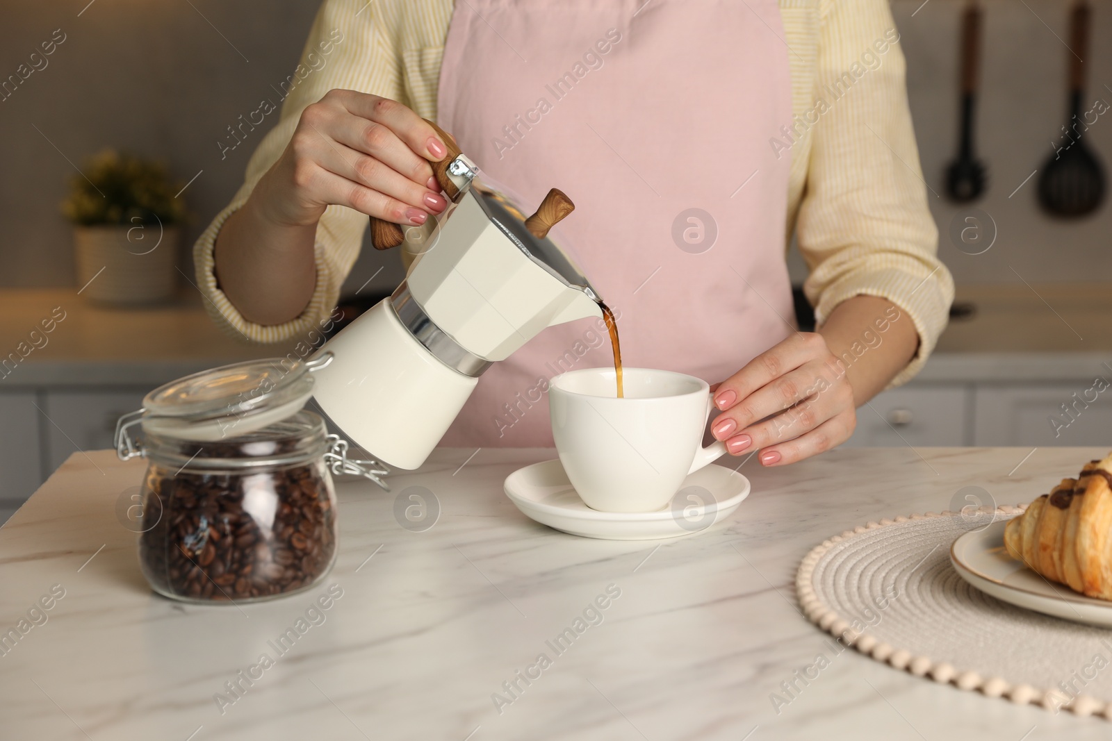 Photo of Woman pouring aromatic coffee from moka pot into cup at white marble table, closeup