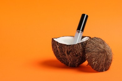 Photo of Tube of eyelash oil and fresh coconut on orange background. Space for text