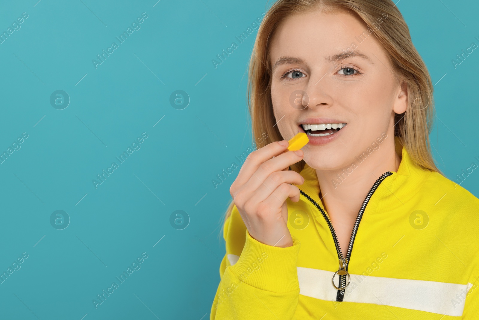 Photo of Woman putting bubble gum into mouth on light blue background. Space for text