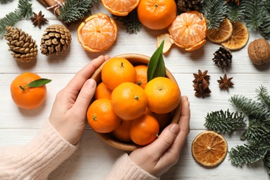 Photo of Woman holding bowl of tangerines at white wooden table, top view. Christmas atmosphere