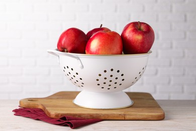 Photo of Fresh apples in colander on white wooden table