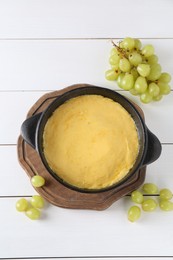 Fondue with tasty melted cheese and grapes on white wooden table, flat lay