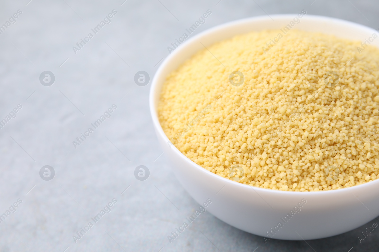 Photo of Raw couscous in bowl on gray table, closeup. Space for text