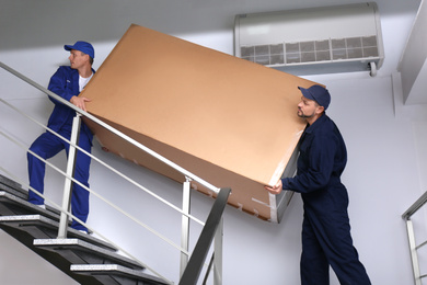 Professional workers carrying refrigerator on stairs indoors