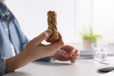 Photo of Woman holding tasty granola bar at light table indoors, closeup. Space for text