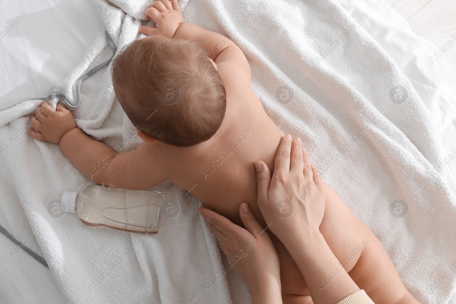 Photo of Mother massaging her baby with oil on towel after bathing, top view