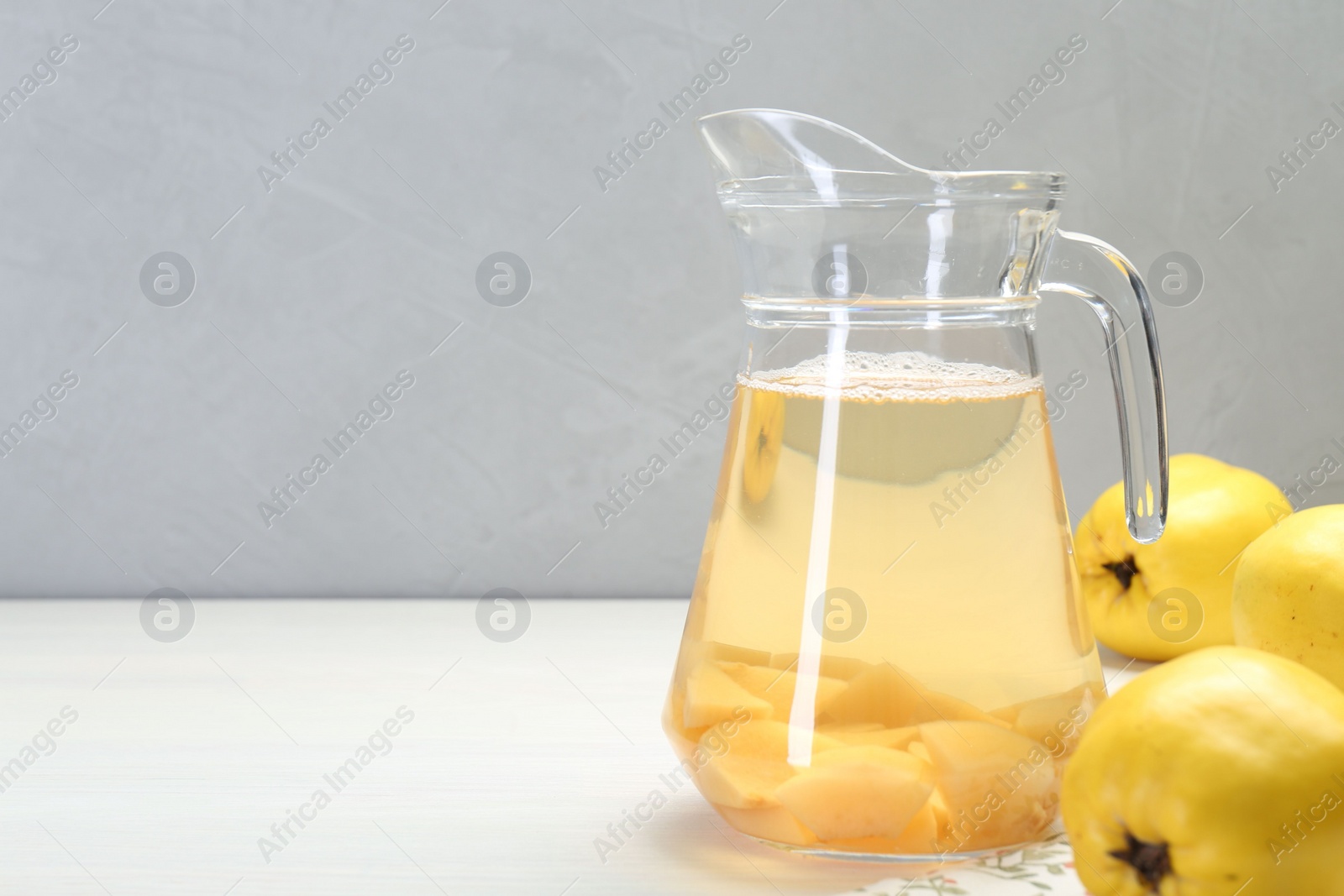 Photo of Delicious quince drink in glass jug and fresh fruits on white wooden table, space for text