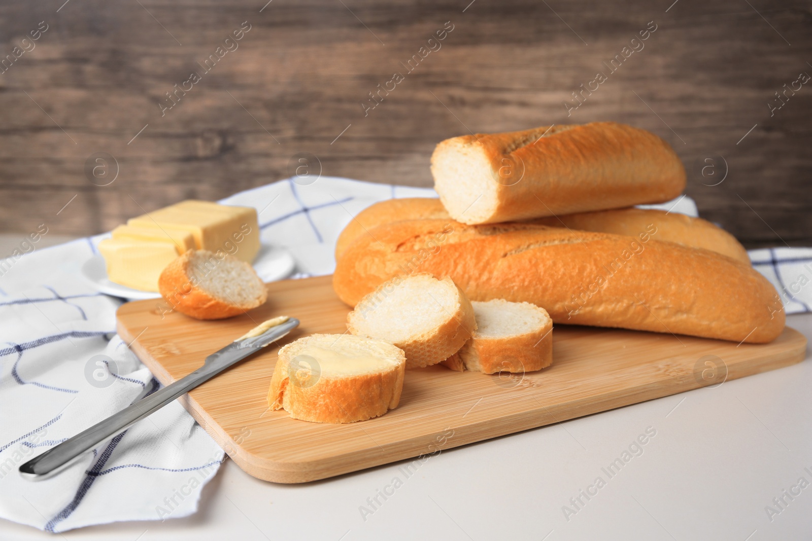 Photo of Tasty cut baguette with fresh butter on white table