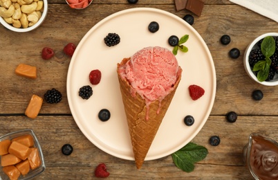 Delicious pink ice cream in wafer cone with berries on wooden table, flat lay