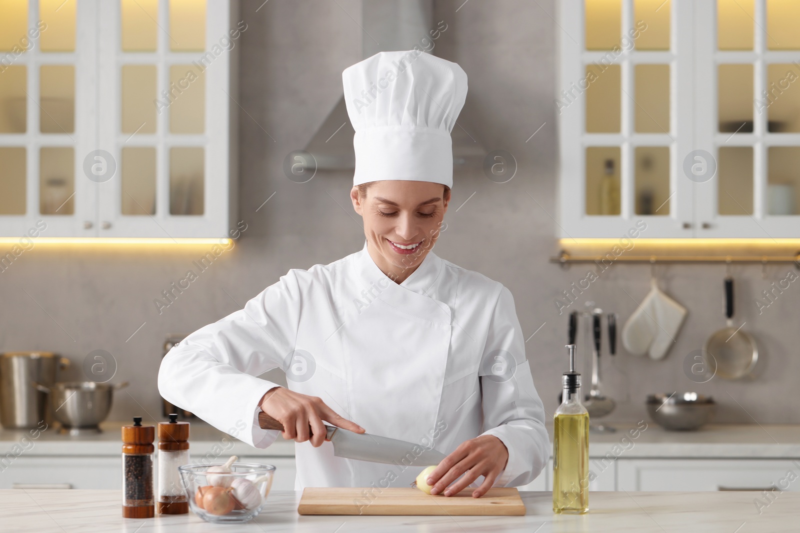 Photo of Professional chef cutting onion at white marble table indoors