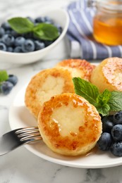 Photo of Delicious cottage cheese pancakes with blueberries, honey and mint on white marble table, closeup