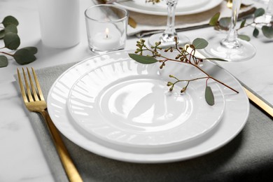 Stylish setting with cutlery and eucalyptus leaves on white marble table, closeup