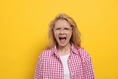Photo of Aggressive young woman screaming on yellow background