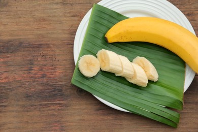 Photo of Plate with delicious bananas and fresh leaf on wooden table, top view. Space for text