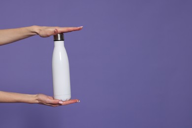 Photo of Woman holding thermos bottle on purple background, closeup. Space for text