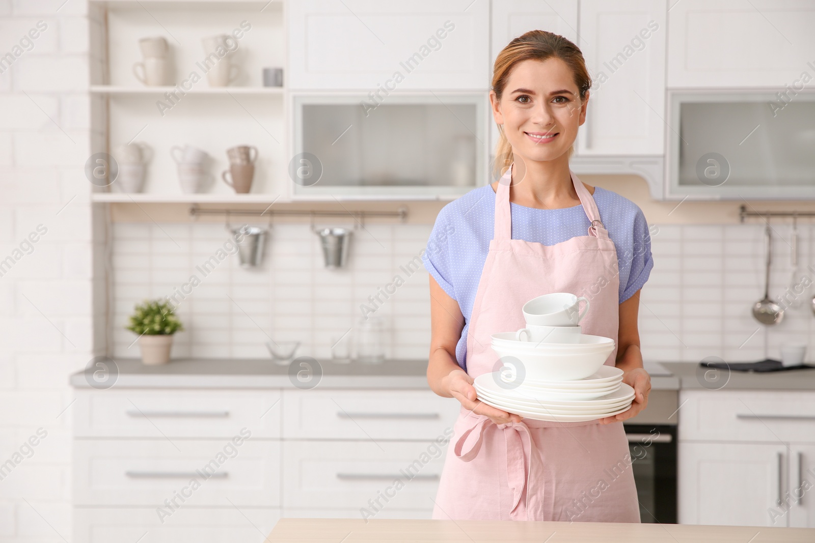 Photo of Woman with clean dishes and cups in kitchen. Space for text