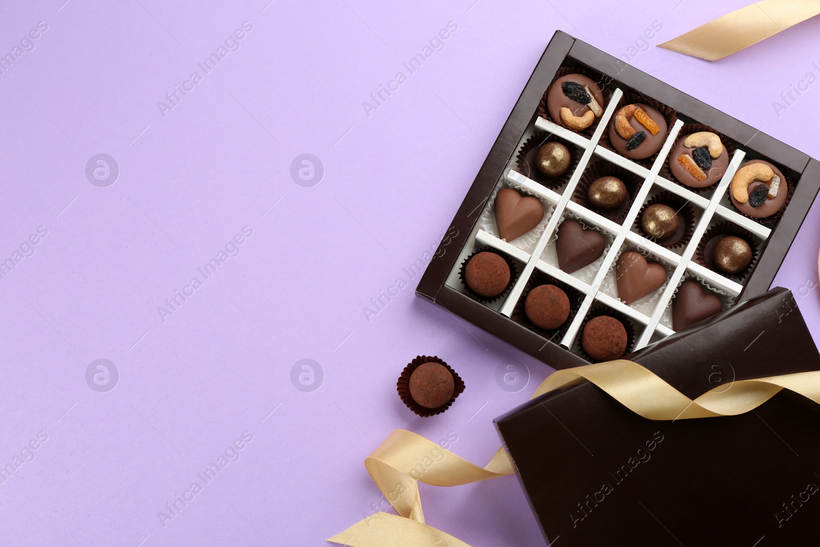 Photo of Different delicious chocolate candies in box and ribbon on lilac background, flat lay. Space for text