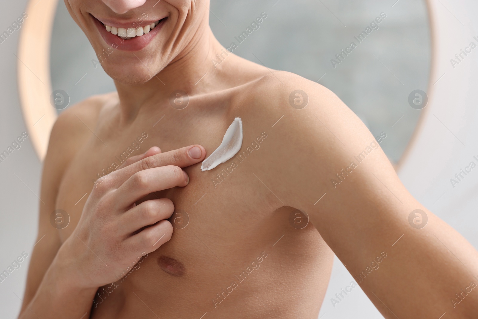 Photo of Man applying moisturizing cream onto his shoulder indoors, closeup