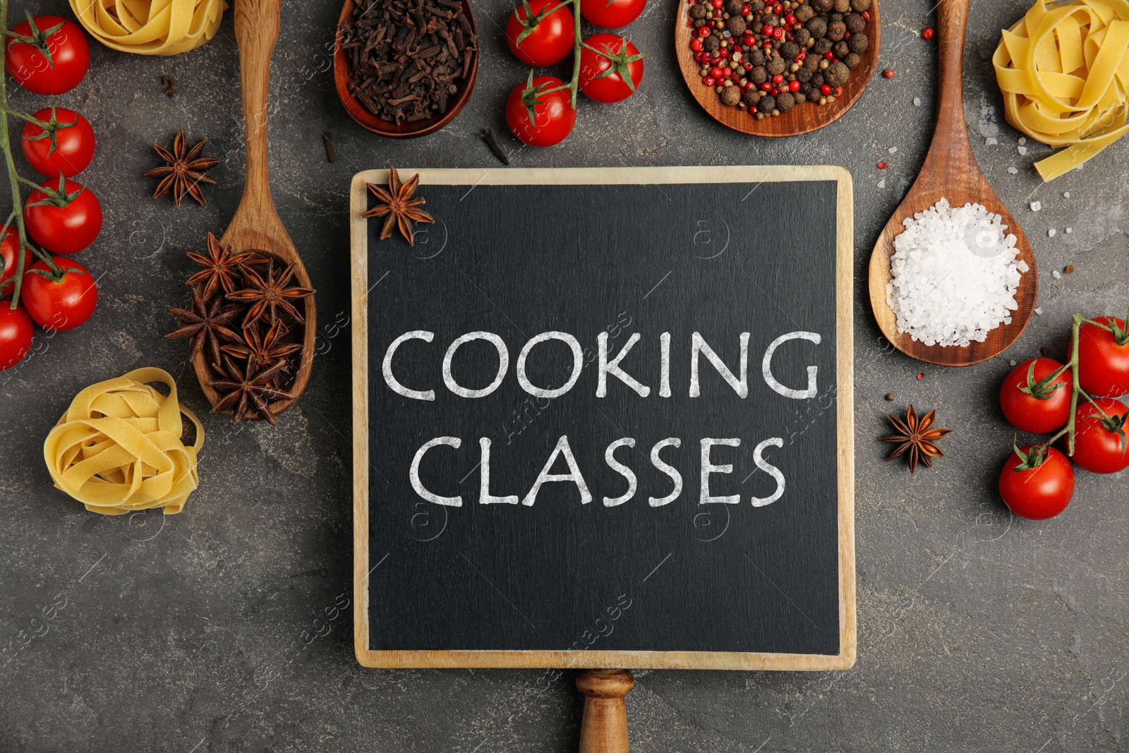 Image of Small chalkboard with inscription Cooking Classes and different fresh products on grey table, flat lay