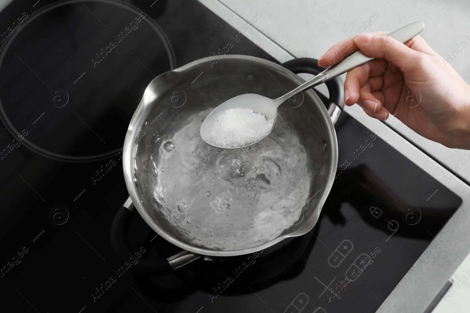 Photo of Woman salting boiling water in pot on stove, top view