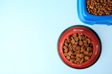 Dry pet food in feeding bowls on light blue background, flat lay. Space for text