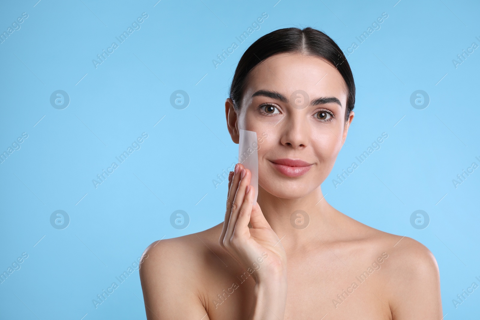Photo of Beautiful woman using mattifying wipe on light blue background, space for text