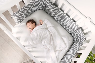 Photo of Cute little baby sleeping in cosy crib indoors