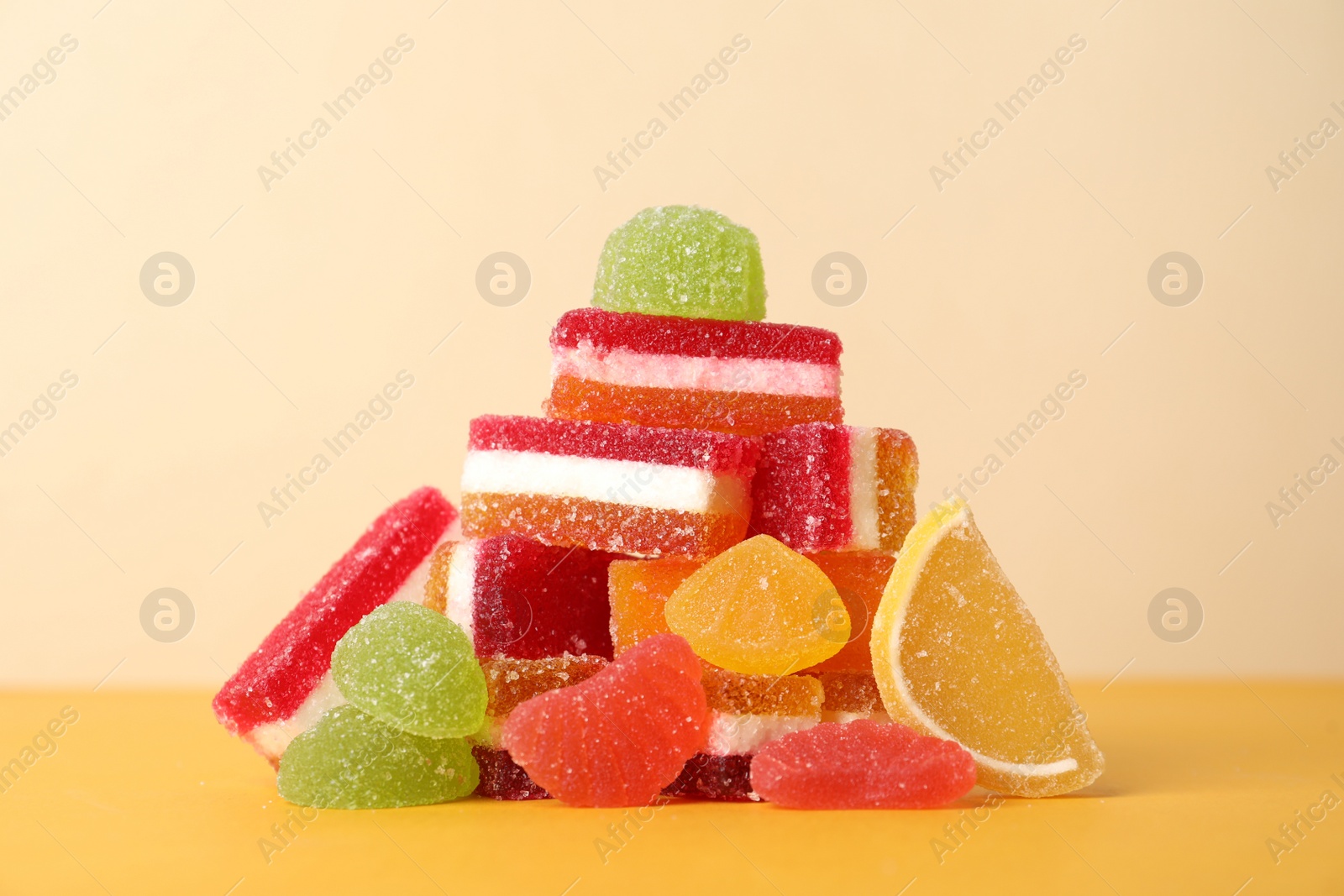 Photo of Pile of delicious bright jelly candies on yellow table