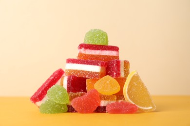 Photo of Pile of delicious bright jelly candies on yellow table