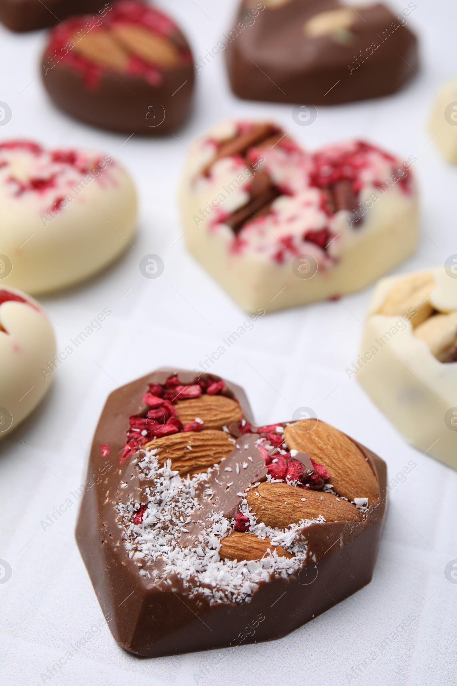 Photo of Tasty chocolate heart shaped candies with nuts on white tiled table, closeup