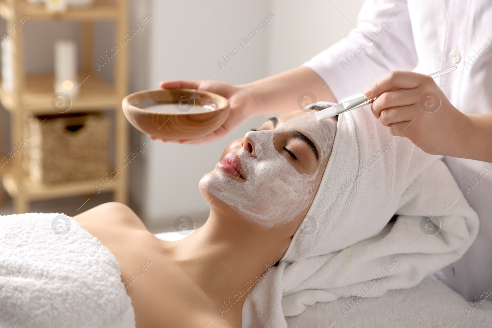 Photo of Cosmetologist applying mask on woman's face in spa salon, closeup