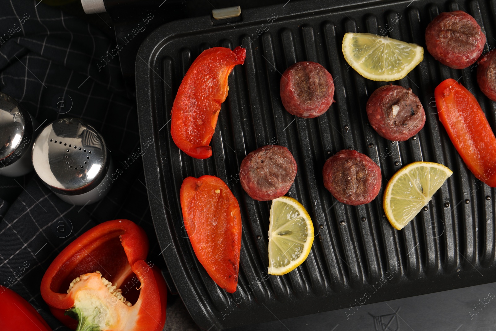 Photo of Electric grill with meat balls, bell peppers and lemon on grey table, flat lay