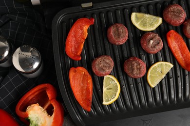 Photo of Electric grill with meat balls, bell peppers and lemon on grey table, flat lay