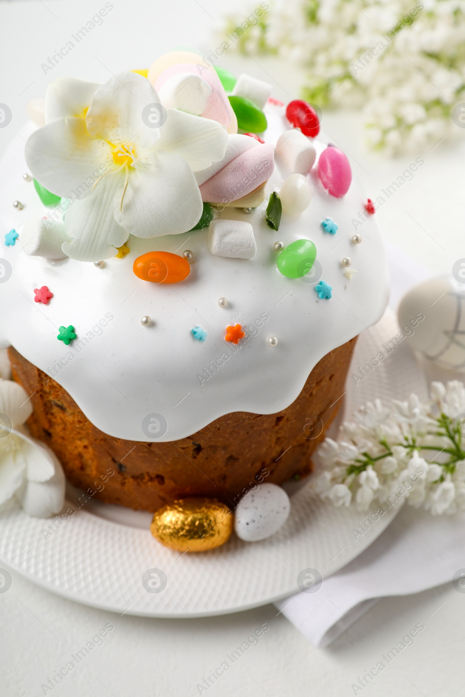 Photo of Traditional Easter cake with sprinkles, jelly beans, marshmallows and decorated eggs on white table, closeup