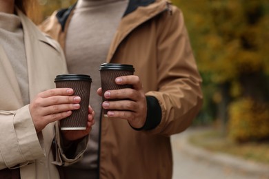 Photo of Happy young couple with cups of coffee spending time together in autumn park, closeup. Space for text