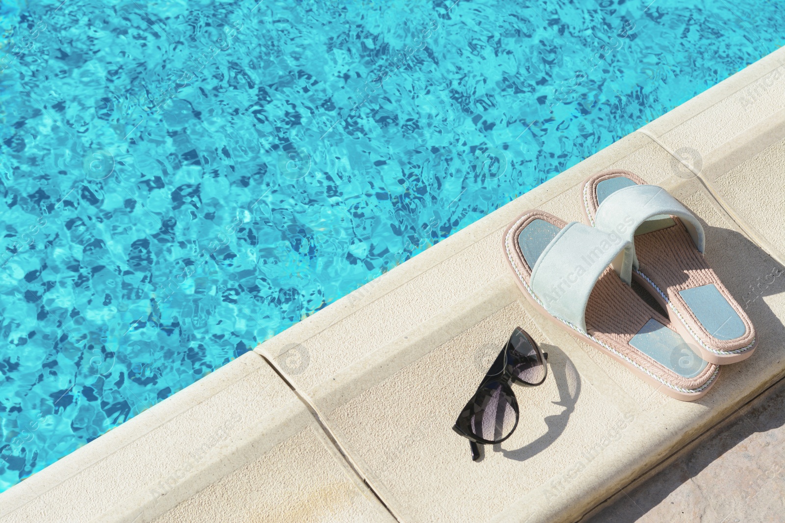 Photo of Stylish sunglasses and slippers at poolside on sunny day, space for text. Beach accessories