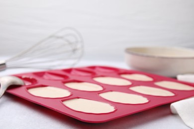 Baking mold for madeleine cookies with batter on white table, closeup