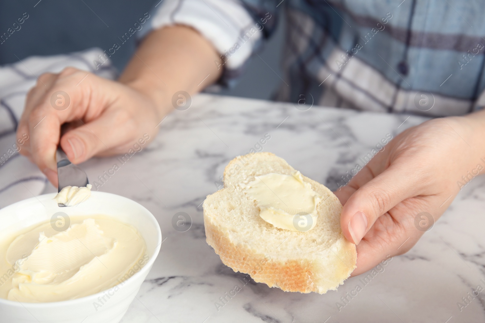 Photo of Woman spreading butter onto slice of bread over marble table, closeup