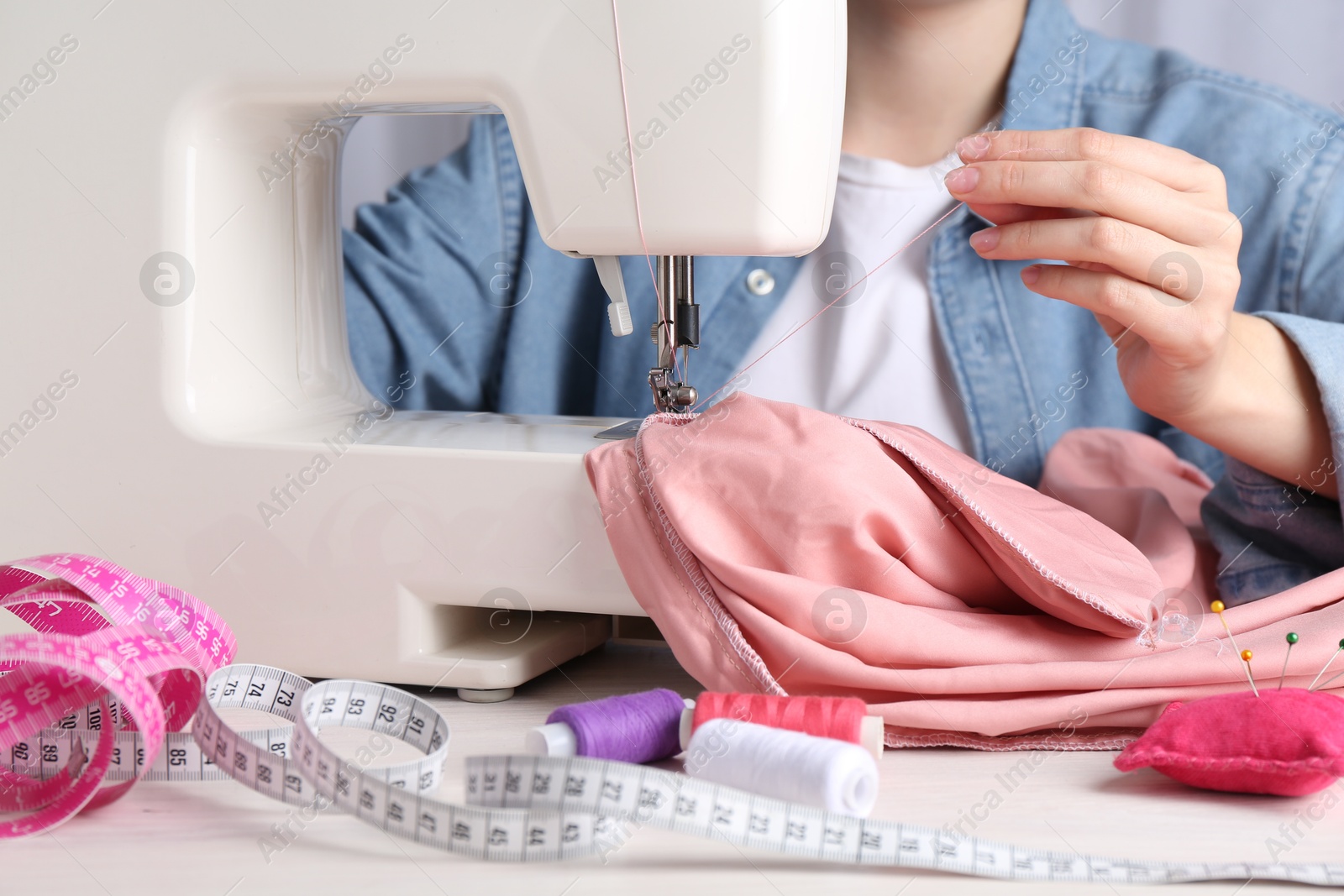 Photo of Seamstress working with sewing machine at white table indoors, closeup