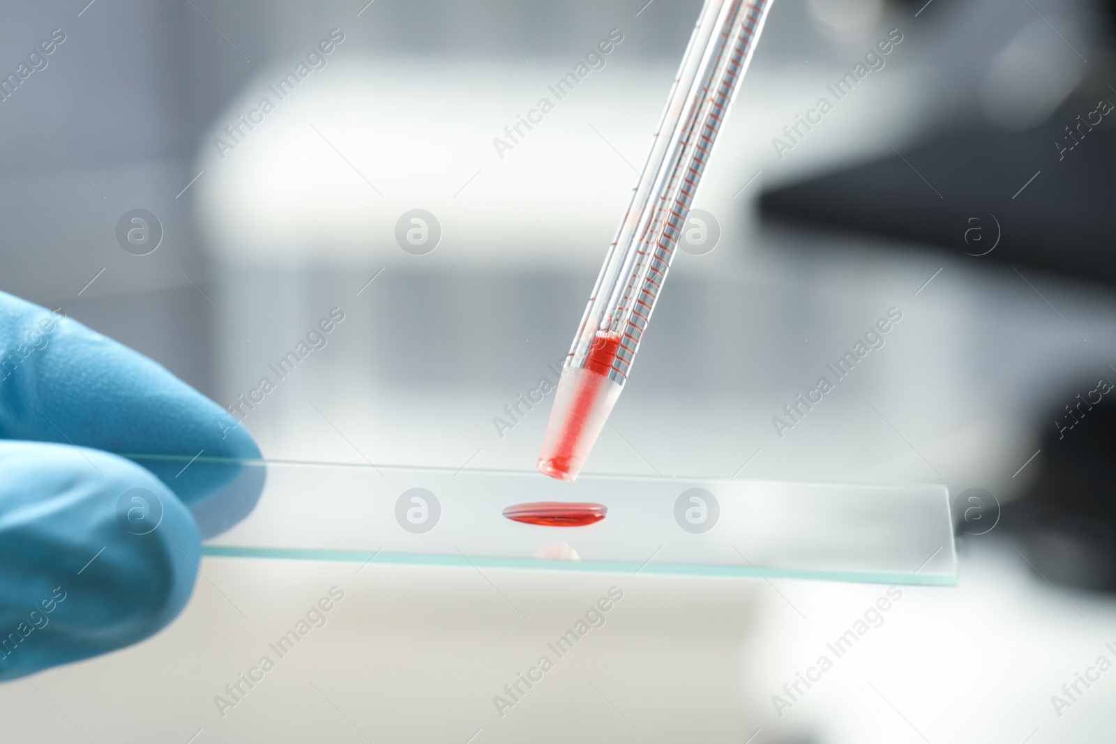 Photo of Scientist dripping sample of red liquid onto microscope slide in laboratory, closeup