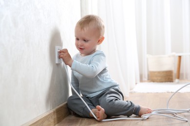 Photo of Little child playing with electrical socket and power strip plug at home. Dangerous situation