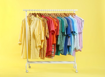 Photo of Bright clothes hanging on rack against yellow background. Rainbow colors