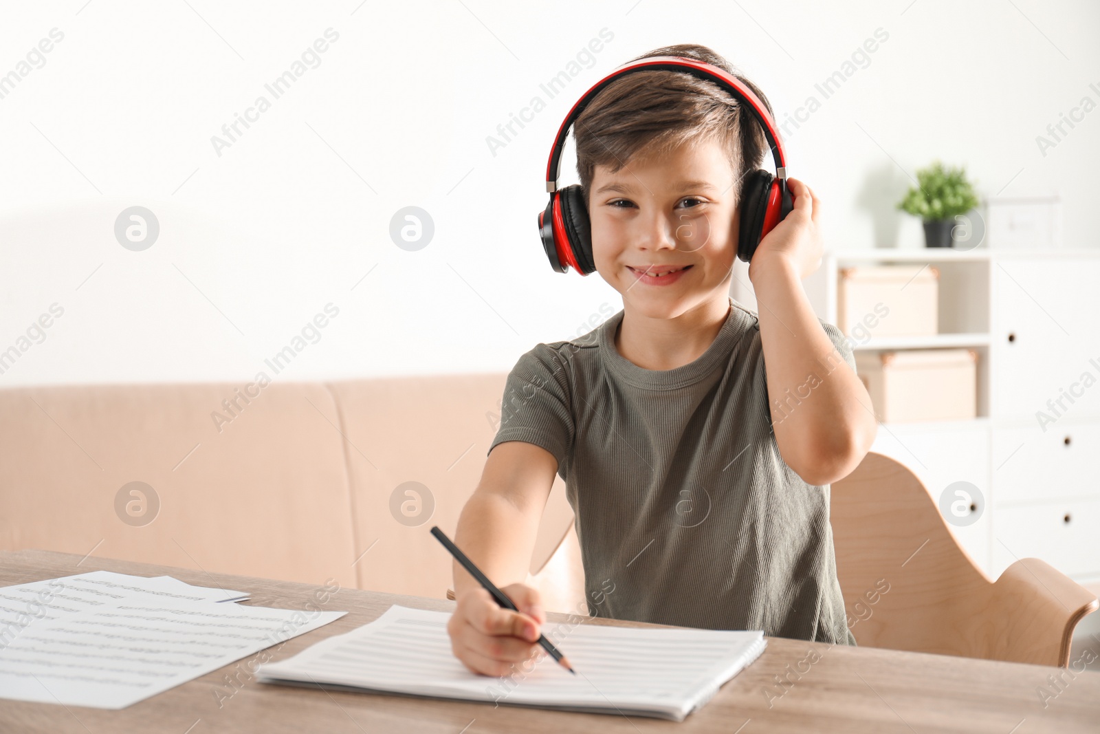 Photo of Little boy writing music notes at table indoors