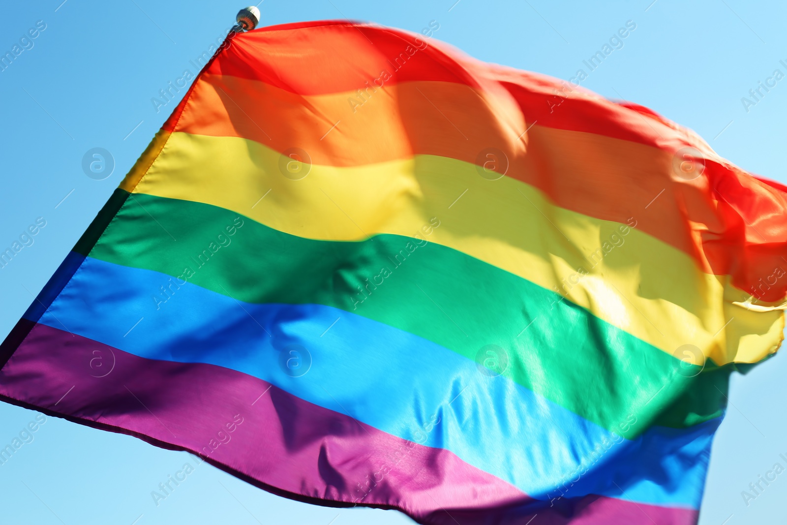 Photo of Rainbow LGBT flag fluttering on blue sky background. Gay rights movement