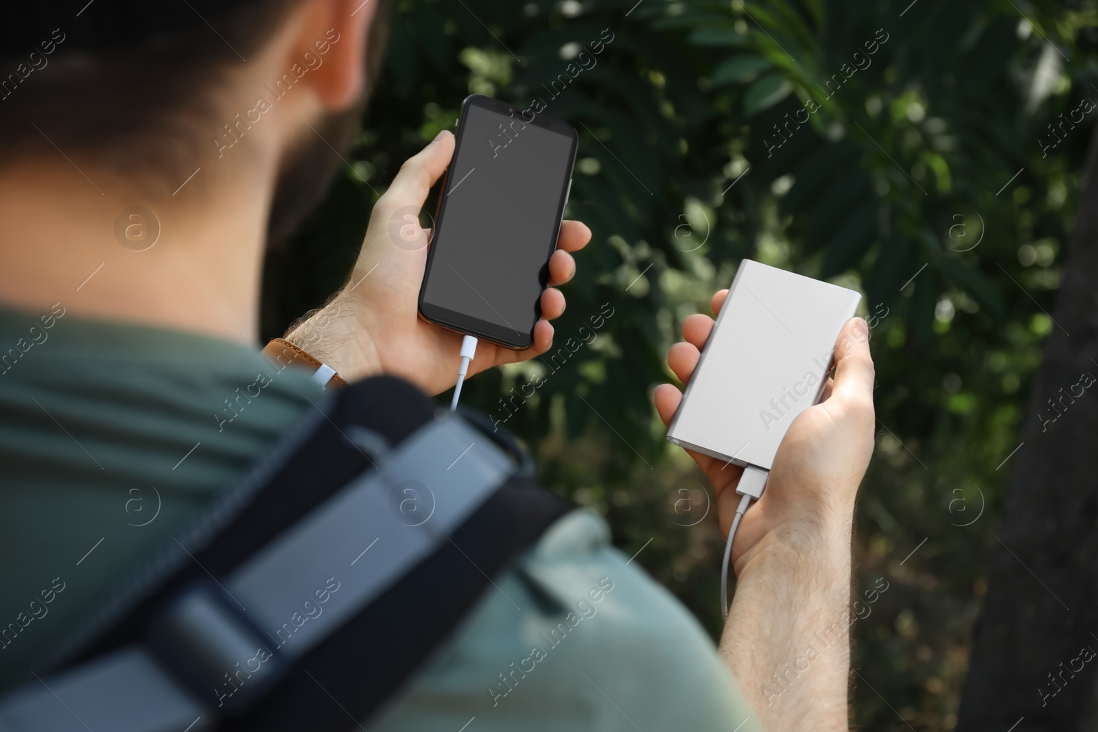 Photo of Man charging mobile phone with power bank in forest, closeup