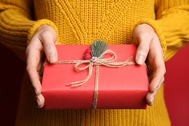 Woman holding Christmas gift box on red background, closeup