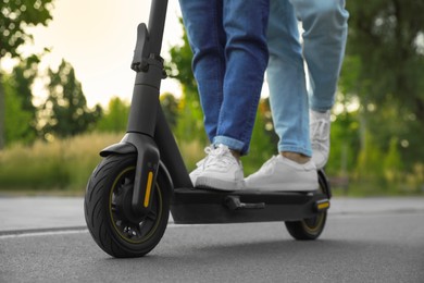 Photo of Couple riding modern electric kick scooter in park, closeup