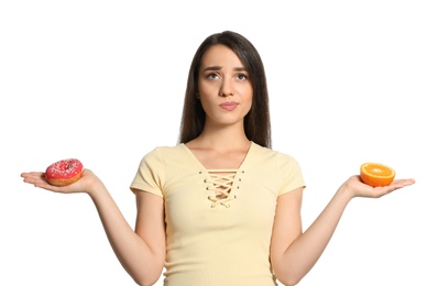 Doubtful woman choosing between orange and doughnut on white background